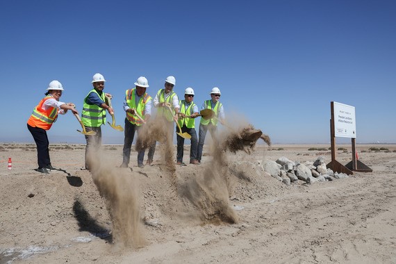 A group of people wearing hard hats and vests toss dirt from a shovel ceremony at the Salton Sea.