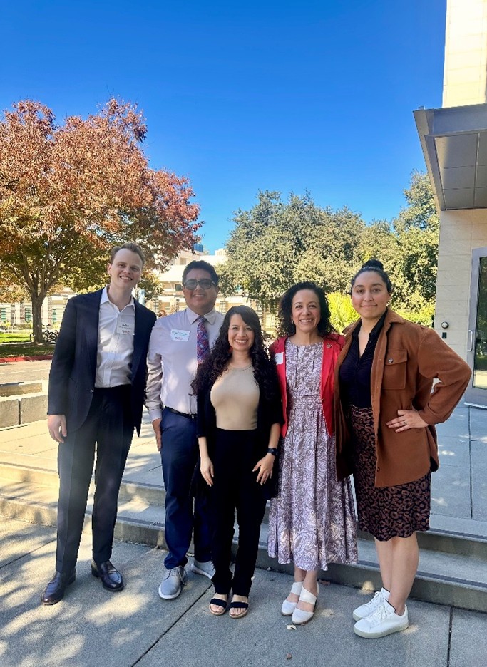a group of five people with trees in the background. From left to right, Joe Shea and Miguel Hernandez, California Natural Resources; Patricia Carrillo, Alianza Coachella Valley; Comissioner Noemí Gallardo, California Energy Commission; Aydee Rodriguez, Alianza Coachella Valley.