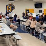 Group of people sitting at the Brawley High School cafeteria facing right towards a presenter